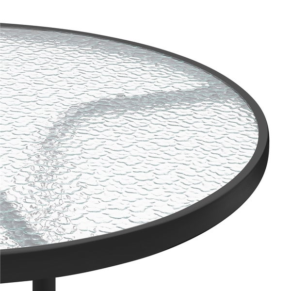 Detailansicht eines runden Tisches mit strukturierter Glasplatte und schwarzem Rahmen.