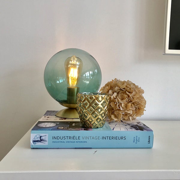 Dekorative Tischleuchte, goldfarbenes Windlicht, Trockenblume und Buch auf einem Tisch