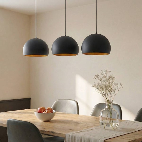 Moderne dreiflammige Pendelleuchte mit mattschwarzen Schirmen und goldener Innenseite über einem Holztisch in einem hellen Esszimmer.