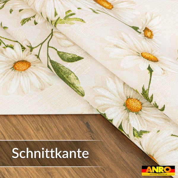 Wachstuch mit Gänseblümchen-Muster auf einer Holzoberfläche, Nahaufnahme der Schnittkante, ANRO Logo.