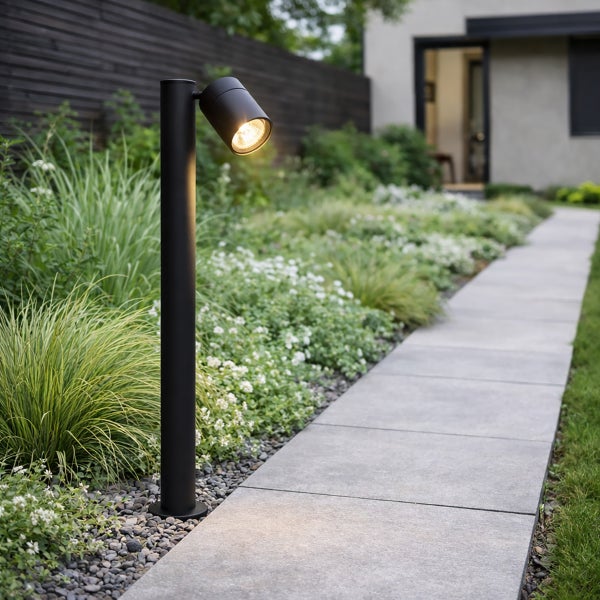 Schwarze Wegeleuchte mit verstellbarem Spot an einem Gartenweg mit Steinplatten und Pflanzen.