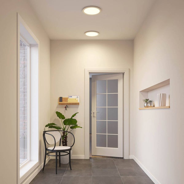 Moderner, heller Flur mit zwei runden LED-Deckenleuchten, einer Glastür, einer Pflanze und einem Stuhl auf Fliesenboden.