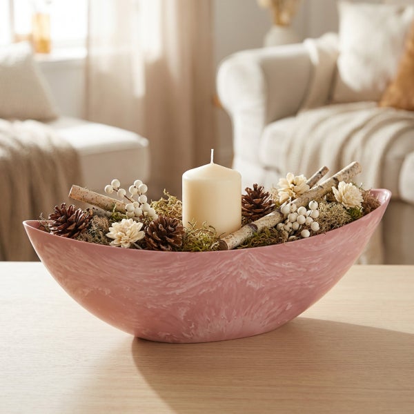 Dekorative Schale mit Kerze und natürlicher Winterdekoration wie Tannenzapfen und Zweigen auf einem Holztisch in einem hellen Wohnraum.