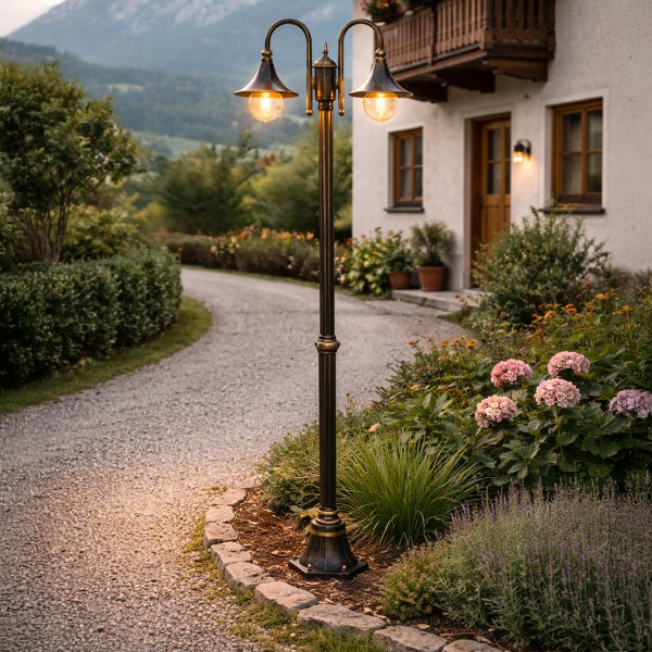Zweiflammige nostalgische Gartenlaterne vor einem Landhausweg mit blühenden Blumenbeeten bei Dämmerung.