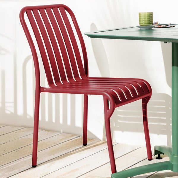 Moderner roter Gartenstuhl aus Metall mit Lattenstruktur auf einer Holzterrasse neben einem Tisch.