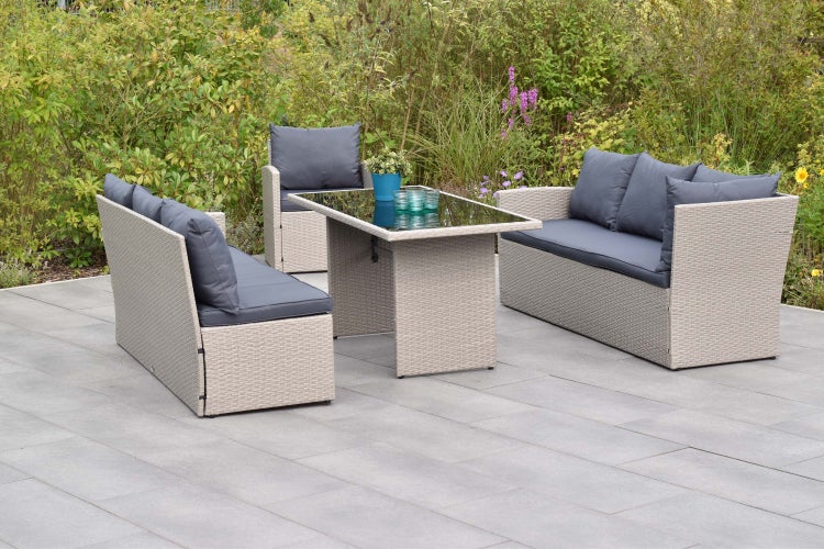Garten-Lounge-Set aus Polyrattan mit zwei Sofas, einem Sessel und einem Tisch mit Glasplatte auf einer Steinterrasse.