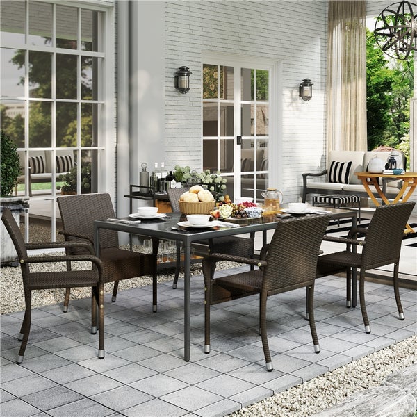 Moderne Terrassen-Essgruppe mit dunklem Glastisch und vier braunen Polyrattan-Stühlen auf einer Terrasse vor einer weißen Ziegelwand.