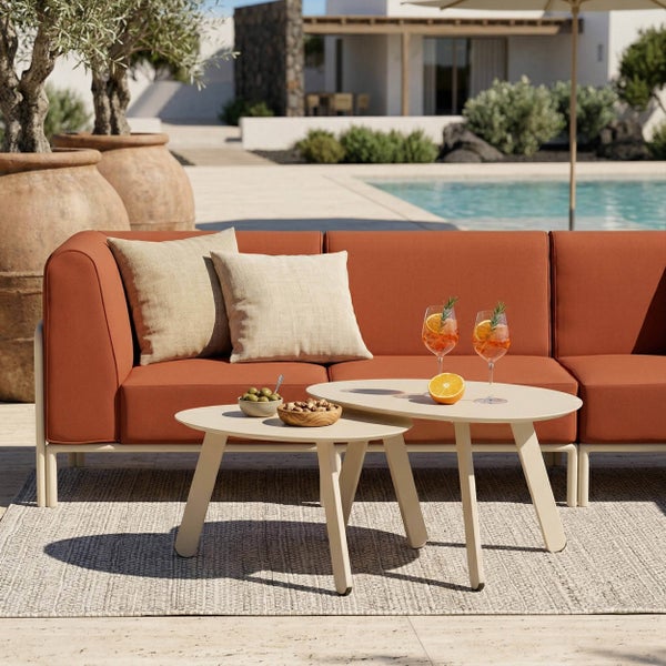 Moderne Gartenlounge mit terracottafarbenem Sofa, beigen Kissen und zwei ovalen Beistelltischen auf einem Außenteppich neben einem Pool.