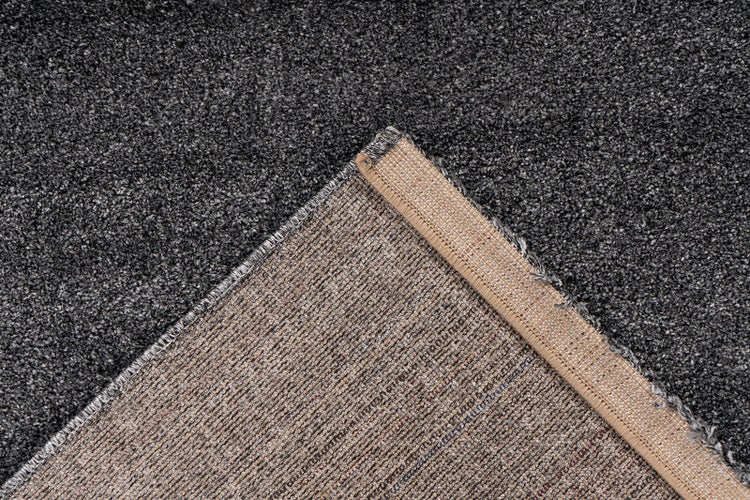 Dunkelgrau melierter Teppichboden mit umgeklappter Ecke, beige Rückseite und geketteltem Rand.