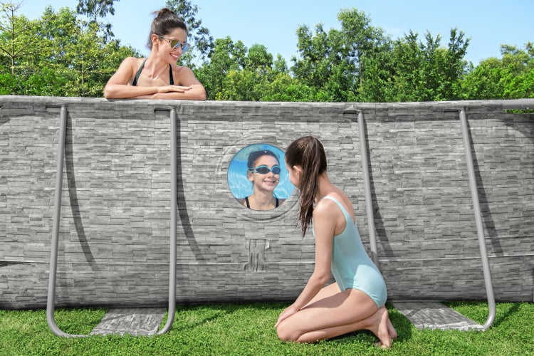Aufstellpool in Steinoptik mit rundem Sichtfenster im Garten, ein Mädchen blickt von außen hinein.