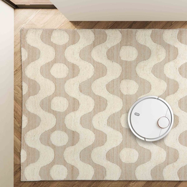 Ein weißer Saugroboter auf einem gemusterten Teppich mit Wellenmuster und Kreisen auf einem Holzboden in der Draufsicht.