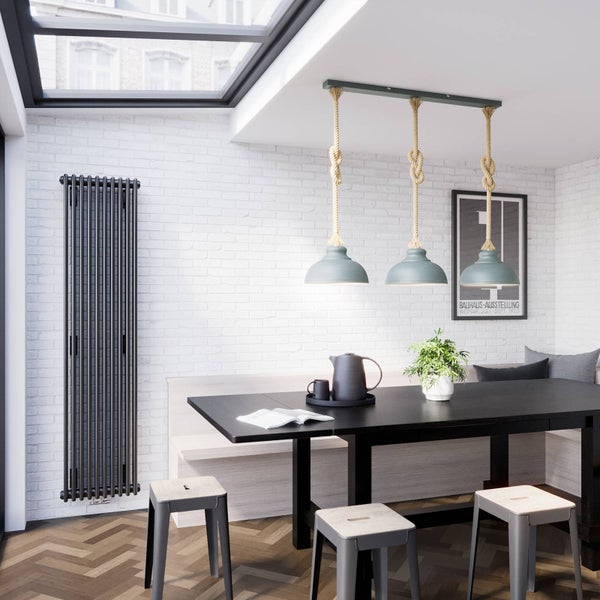 Vertikaler Design-Heizkörper mit Rundrohren an einer weißen Ziegelwand in einem modernen Esszimmer mit schwarzem Tisch und Seil-Pendelleuchten.