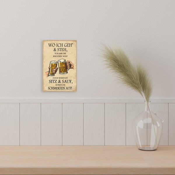 Wandbild mit Biermotiv und Spruch in heller Atmosphäre über einer Holzoberfläche neben einer Glasvase mit Trockengras.