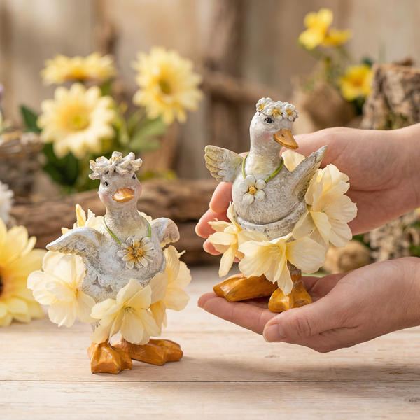 Zwei Deko-Enten-Figuren mit Blumenkronen und Röcken aus Blüten, Frühlings- und Osterdekoration.