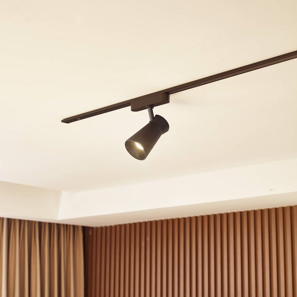 Schwarzer Schienensystem-Strahler an einer Deckenschiene in einem hellen Raum mit moderner Holzlamellenwand.