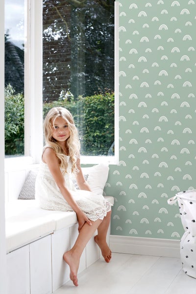 Mädchen sitzt auf Fensterbank vor Tapete mit Regenbogenmuster