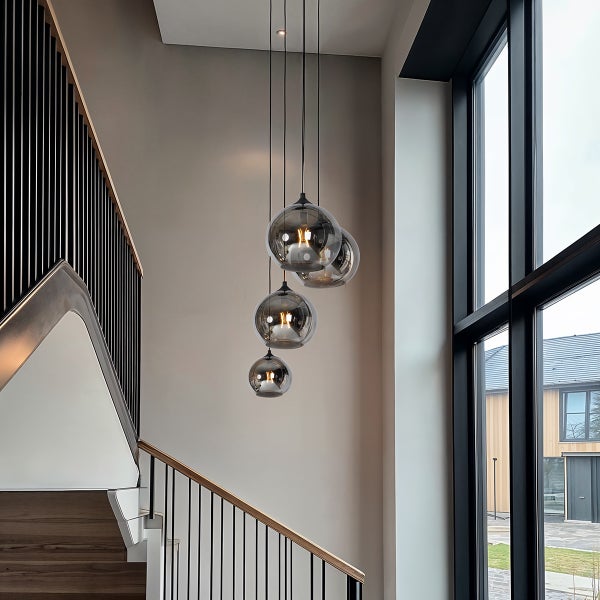 Moderne Treppenhausbeleuchtung mit vier kugelartigen Pendelleuchten aus Glas in verschiedenen Höhen neben einem großen Fenster.
