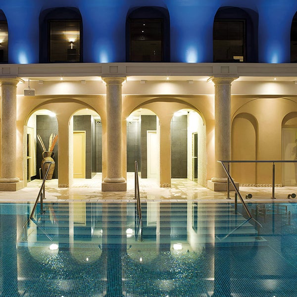 Innenpool mit Mosaikfliesen und eleganten Säulen in einem Wellnessbereich mit architektonischen Torbögen und stimmungsvoller Beleuchtung.