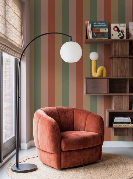 Wohnzimmer mit gestreifter Tapete, einem samtigen Sessel, einer Bogenlampe und einem Holzregal im modernen Einrichtungsstil.