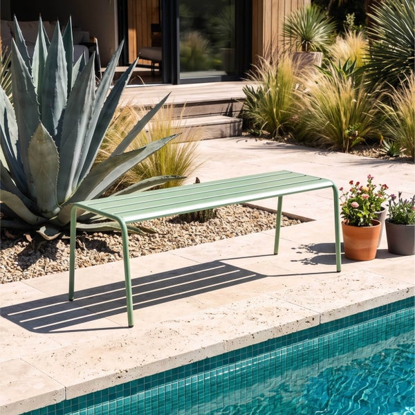 Moderne grüne Gartenbank aus Metall auf einer hellen Terrasse am Pool, umgeben von einer Agave und Gräsern in einem modern gestalteten Außenbereich.