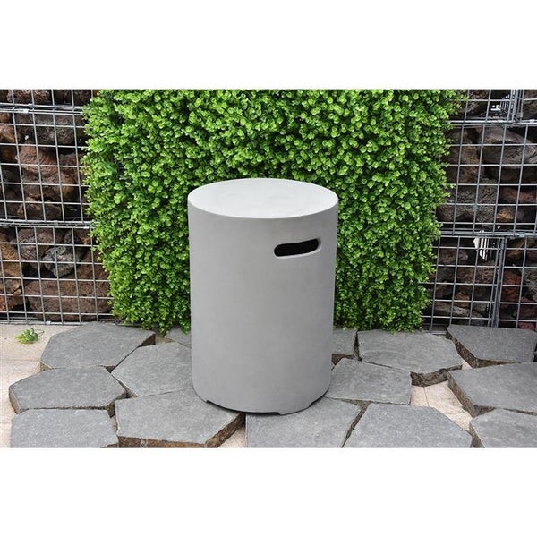 Zylindrischer Gartenhocker aus Faserzement in Betonoptik mit Griffmulde auf Steinplatten vor einer Hecke und Gabionenwand.
