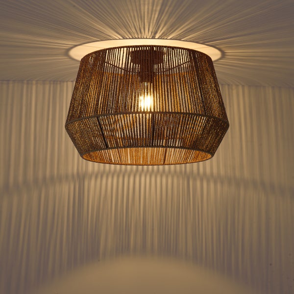 Eingeschaltete Deckenleuchte aus Papierseil-Geflecht, die ein dekoratives Streifenmuster aus Licht und Schatten an Wand und Decke wirft.