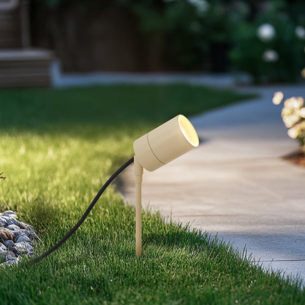 Gartenstrahler mit Erdspieß beleuchtet einen gepflasterten Gartenweg von einer Rasenfläche aus.
