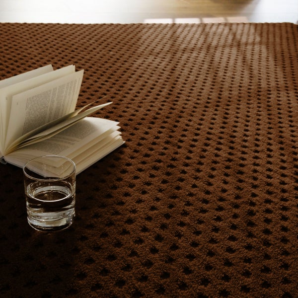 Strukturierter Teppichboden mit Noppenmuster, darauf ein aufgeschlagenes Buch und ein Glas Wasser in wohnlicher Atmosphäre.