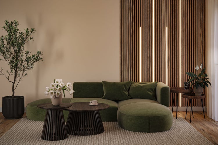 Modernes Wohnzimmer mit grünem Sofa, Wandpaneelen aus Holzlatten mit LED-Streifen, dunklen runden Couchtischen und Zimmerpflanzen auf hellem Teppich.
