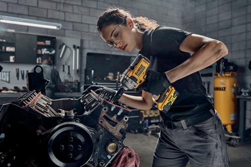 Frau arbeitet mit einem DeWalt Schlagschrauber an einem Motorblock in einer Werkstatt.
