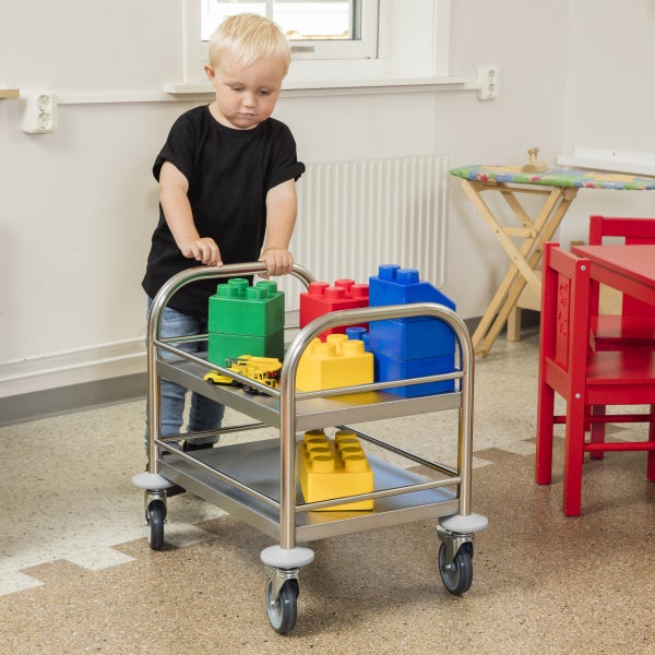 Ein Kind schiebt einen Servierwagen mit Spielzeug im Raum.