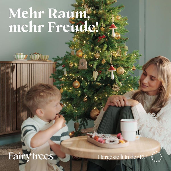 Mutter und Kind vor einem beleuchteten Fairy Trees Weihnachtsbaum mit Dekoration in einem wohnlich eingerichteten Zimmer.