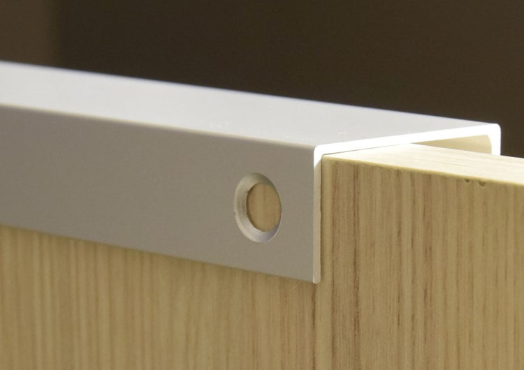 Detailaufnahme eines Möbelgriffs aus Metall an einer Holzschublade.