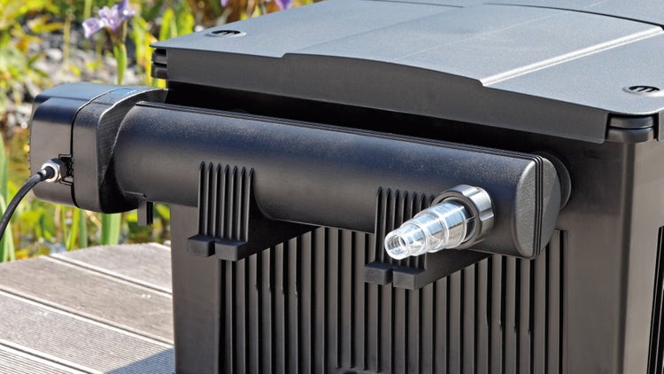 Schwarzes Teichfiltersystem mit UVC-Klärer und transparentem Schlauchanschluss auf einem Holzsteg im Garten.