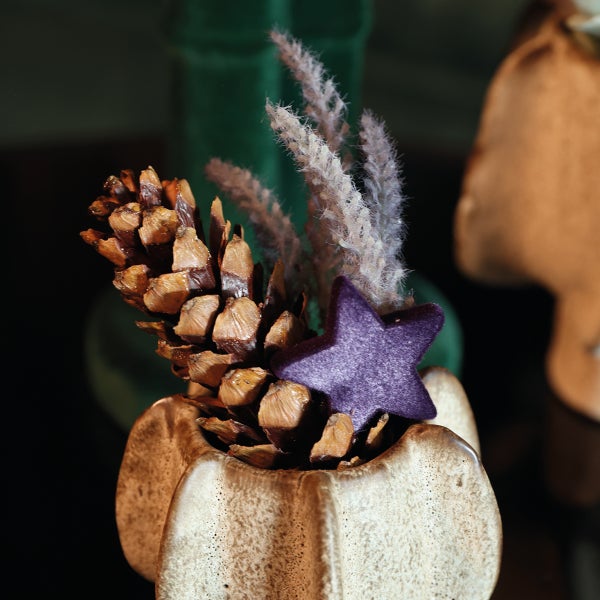 Weihnachtliche Tischdekoration mit Tannenzapfen, Trockenblumen und Stern in einer strukturierten Vase.