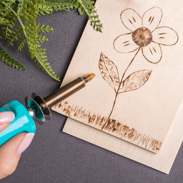 Schwarze Kreidetafel zum Aufhängen mit der weißen Aufschrift Home Sweet Home und einer Hauszeichnung neben Trockenblumen.