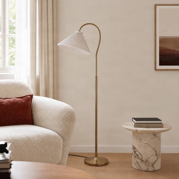 Moderne Stehlampe mit geschwungenem Metallständer und plissiertem Lampenschirm in einem stilvoll eingerichteten Wohnzimmer.