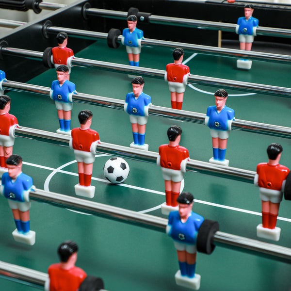 Nahaufnahme eines Tischfußballspiels mit roten und blauen Spielfiguren auf einem grünen Feld mit einem Fußball.