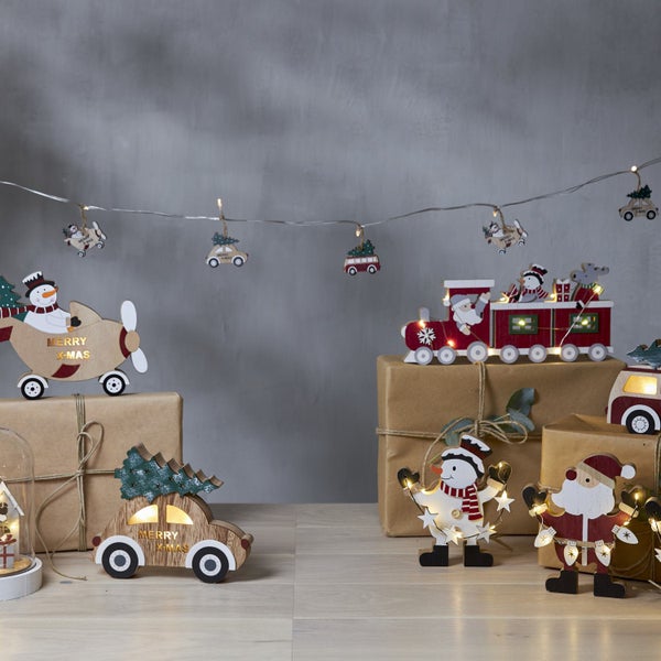Weihnachtliche Dekoration mit verschiedenen Holzfiguren, darunter Zug, Flugzeug, Auto, Weihnachtsmann und Schneemann