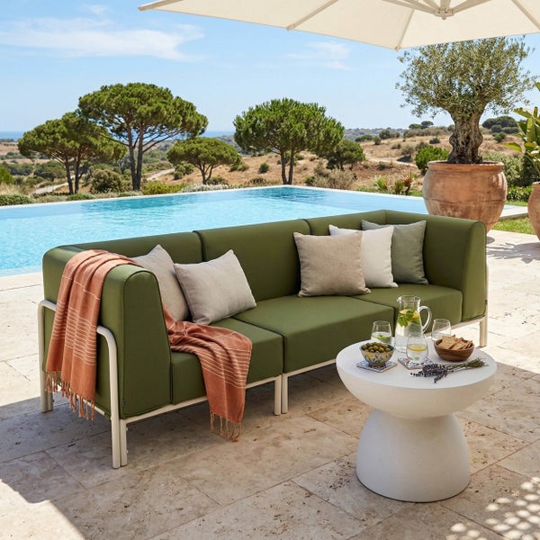Modernes Garten-Lounge-Set mit grünem Loungesofa mit Metallgestell und weißem Beistelltisch auf einer Steinterrasse am Pool.