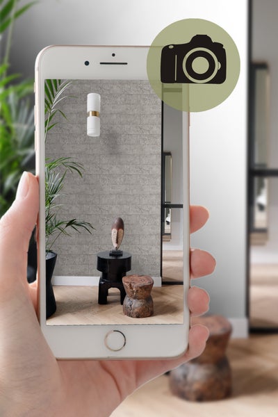 Nahaufnahme eines Smartphones, das ein Interieur mit Wandleuchte, Dekoration und Möbeln zeigt