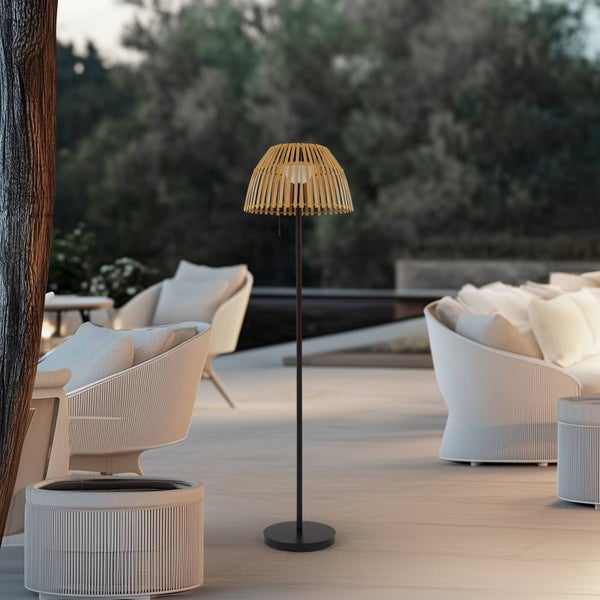 Moderne Outdoor-Stehleuchte mit Schirm aus Holzlamellen und schwarzem Gestell auf einer Terrasse mit Loungemöbeln.