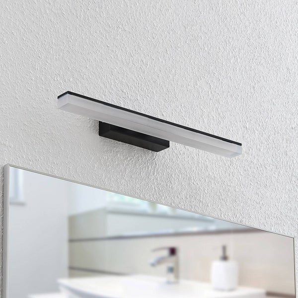 Moderne schwarze LED-Spiegelleuchte an einer weißen strukturierten Wand über einem Badezimmerspiegel montiert.