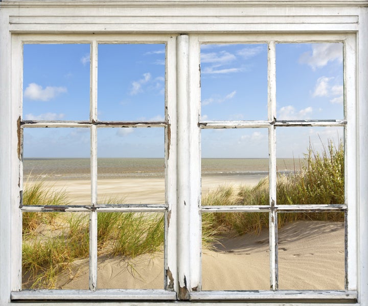 Blick durch ein altes Fenster auf einen Sandstrand