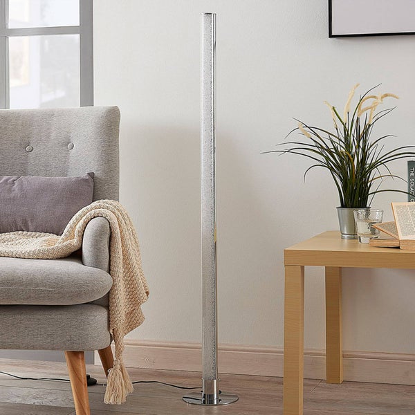 Schlanke LED-Stehleuchte in Säulenform mit Kristall-Effekt neben einem Sessel in einem hellen Wohnzimmer.