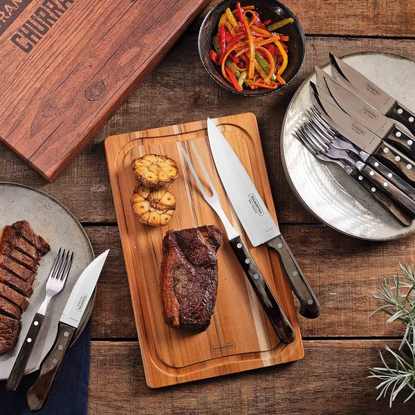 Tisch gedeckt mit Steak, gegrilltem Knoblauch, Salat und Tramontina Churrasco Grillbesteck auf Holz