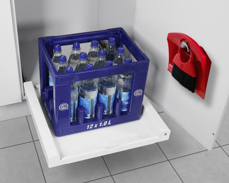 Weißer Tablarauszug im Küchenunterschrank mit einem blauen Getränkekasten für 12 Flaschen zu je 1 Liter und einem roten Kehrset an der Schranktür.