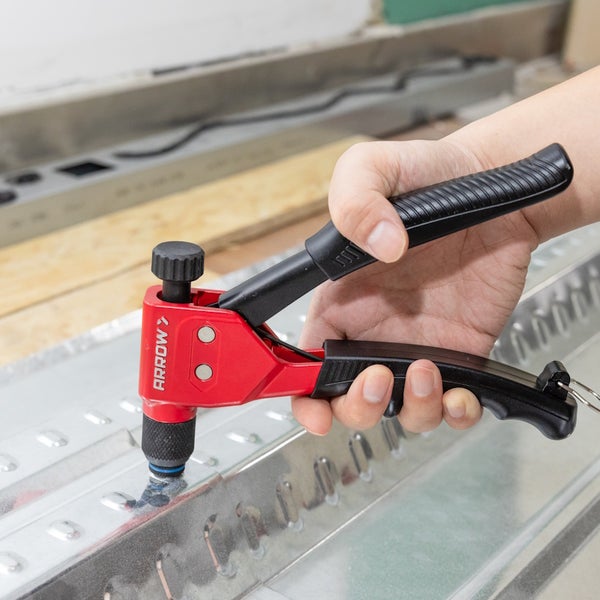 Hand bedient eine rot-schwarze Blindnietzange von Arrow, um Metallprofile in einer hellen Werkstatt miteinander zu verbinden.