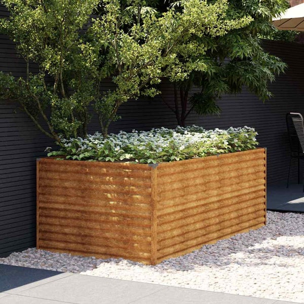 Rechteckiges Hochbeet aus Metall in Rostoptik mit Wellenprofil, bepflanzt mit weißen Blumen und einem Baum in einem modernen Garten auf Kies.