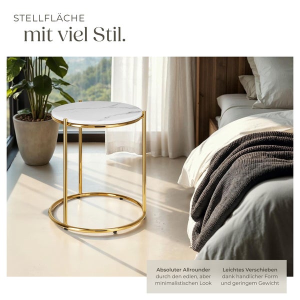 Minimalistischer Beistelltisch in Marmoroptik mit Goldgestell in hellem Schlafzimmer neben einem Bett und einer Zimmerpflanze.